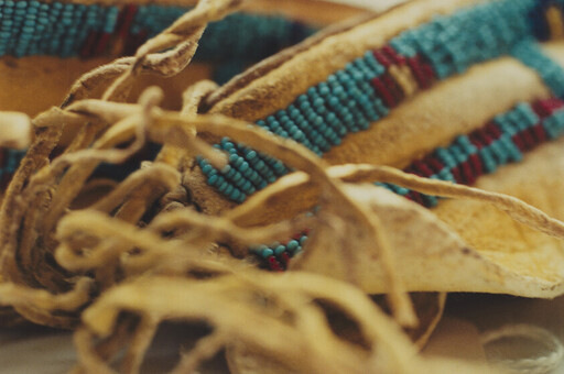 Soft leather moccasins with turquoise and red beadwork and knotted leather laces resting close up.