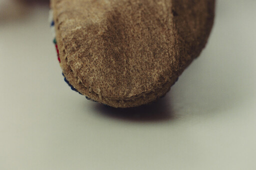 Close-up of a brown suede slipper toe with visible hand stitching and colorful trim.