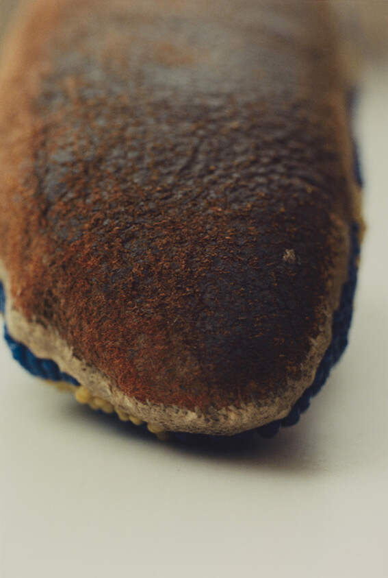 Worn brown suede shoe toe with frayed stitching and scuffed surface resting on a light background.
