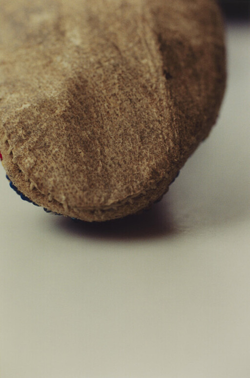 A close-up of the rounded brown felt toe of a small slipper resting on a light surface.