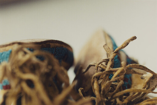 Worn leather moccasins with tangled frayed laces and blue beadwork lie close together.