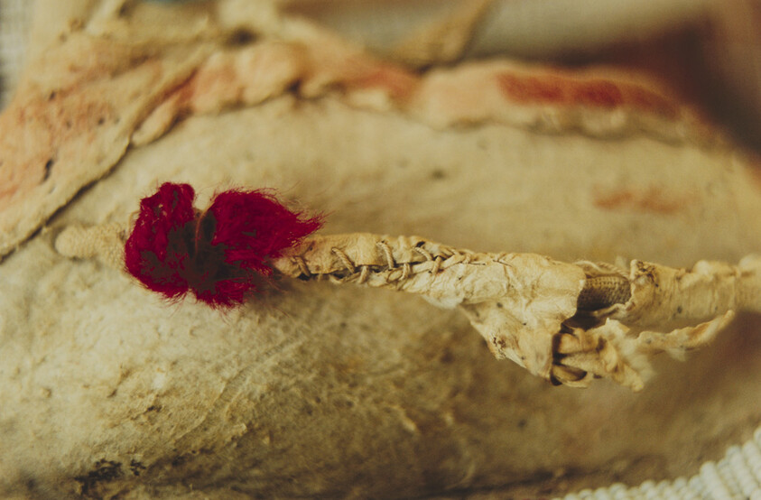 Close-up of a worn stitched leather seam on a moccasin with a small red yarn tuft.