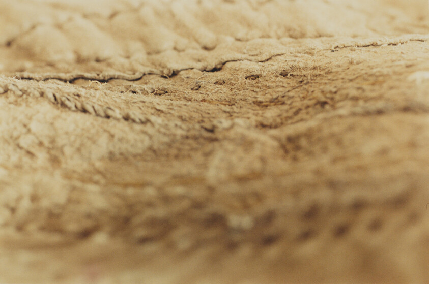 Close-up of soft tan fabric showing fuzzy texture and a visible stitched seam.