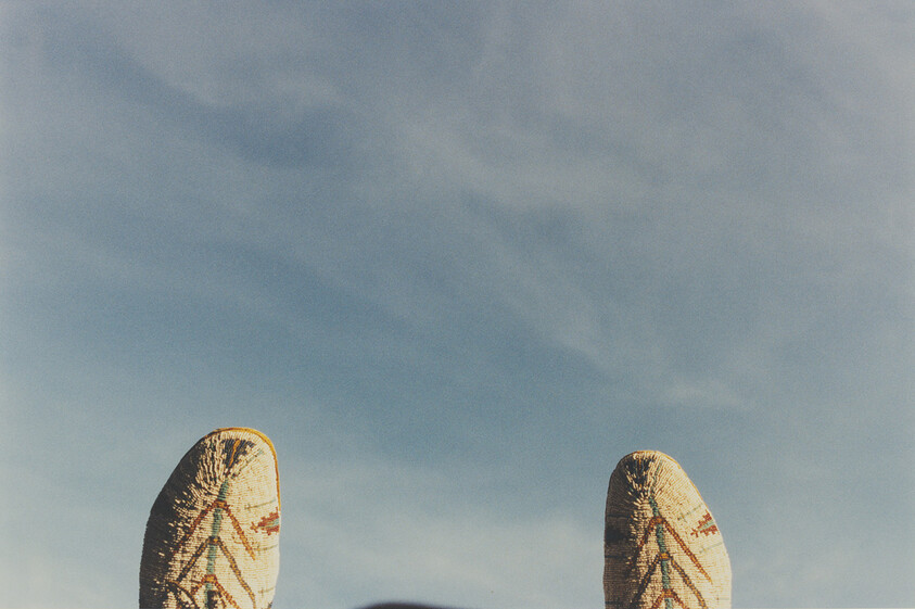 Person's patterned cowboy boots point upward against a clear blue sky.
