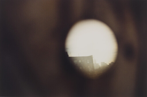 A circular peephole view reveals a distant city building silhouette through soft, warm blur.