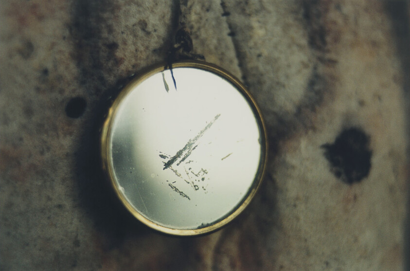 Close-up of a scratched round mirror reflecting light, set against a grungy background.