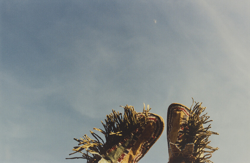 Worn fringe moccasin boots kicked up against a clear blue sky.