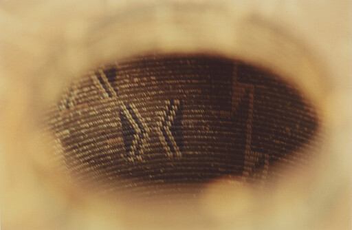 View through a circular opening showing a woven fabric pattern with light brown tones.