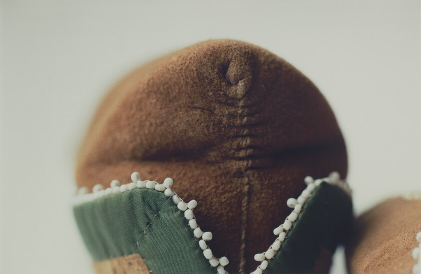 Brown cloth doll head with a green fabric collar trimmed in small white bead decorations.