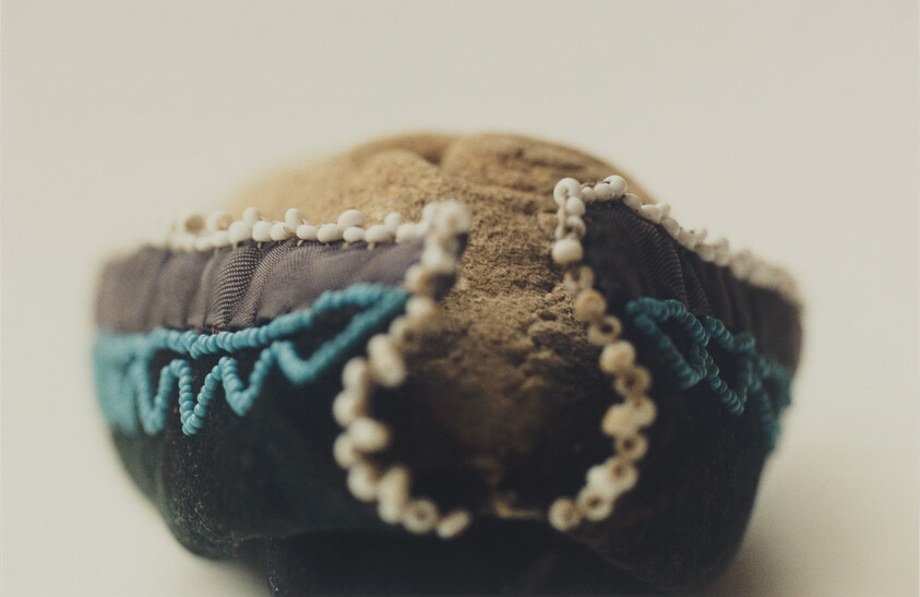 Small fabric pincushion with turquoise zigzag stitching and a beaded edge resting on a light surface.