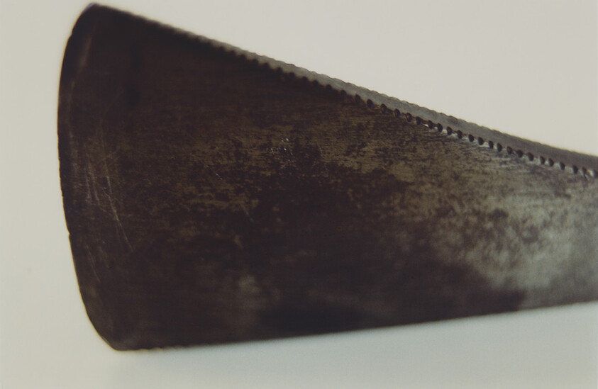 Close-up of a worn, rusted serrated metal blade edge resting on a light surface.