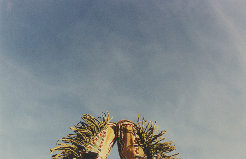 Two decorated moccasin boots with fringe pointed upward against a clear blue sky.