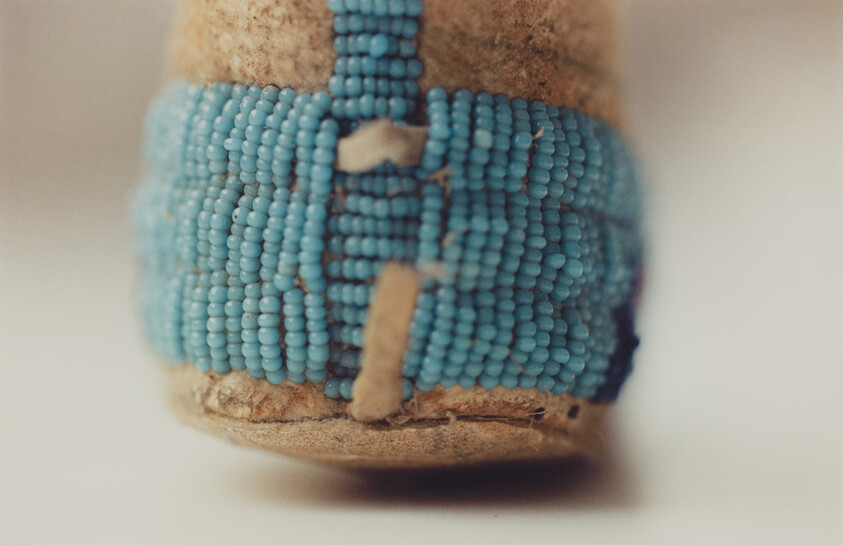 Close-up of a leather moccasin toe with worn turquoise beadwork and hand-stitched detailing.
