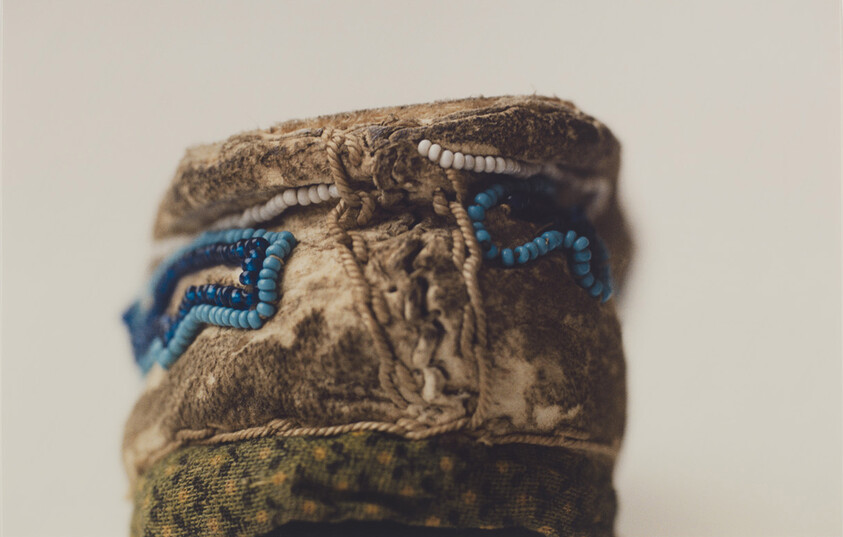 Worn beaded moccasin cuff with blue and white beadwork and frayed stitched leather edges.