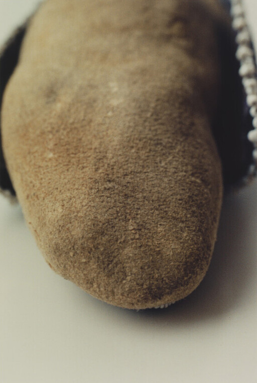 Close-up of a worn brown suede slipper toe showing soft texture and side stitching.