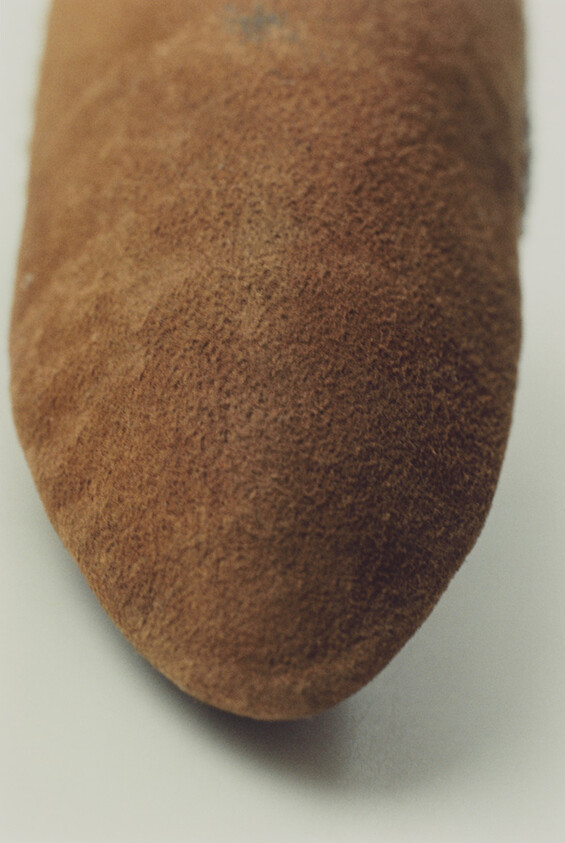 Brown suede shoe toe with fine nap and slightly rounded point on a light background.
