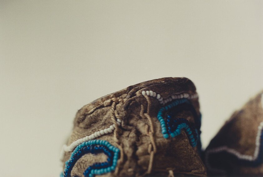 Brown suede moccasin with blue and white beadwork detail on the toe.