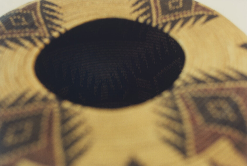 A woven basket with a dark central opening and geometric patterned sides.
