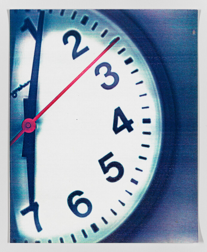 A close-up view of a clock face showing the time at ten minutes past ten with a red second hand, black minute hand, and black hour hand against a white background with numbers 2 through 6 visible. The image has a bluish tint and appears slightly overexposed, giving it a dreamy quality.