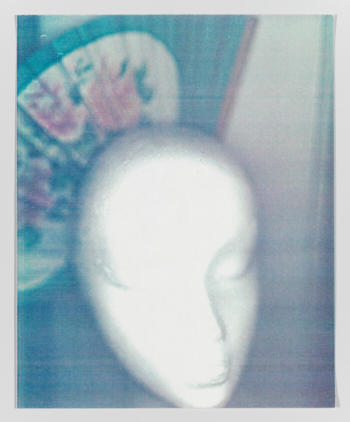 Blurred image of a white mannequin head with indistinct colorful background.