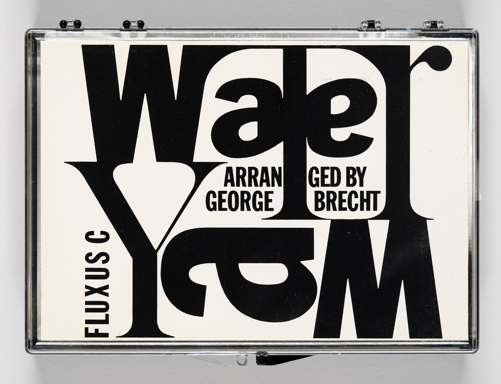 A graphic art piece with bold black typography on a white background, encased in a clear frame. The text is a playful arrangement of letters and words, including "Water Yam," "Arranged by George Brecht," and "Fluxus," creating a dynamic and abstract composition.
