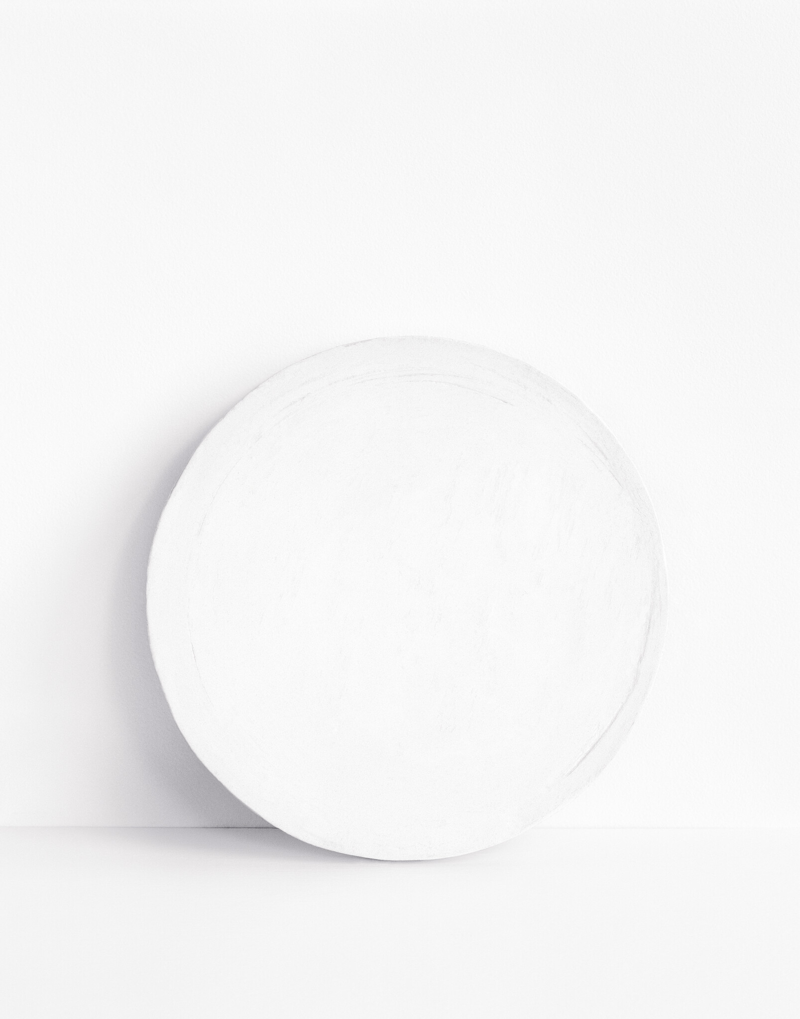 Large round white disc leaning against a white wall on a white surface.