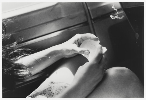 A person holds and reads a small folded note while seated by a window.