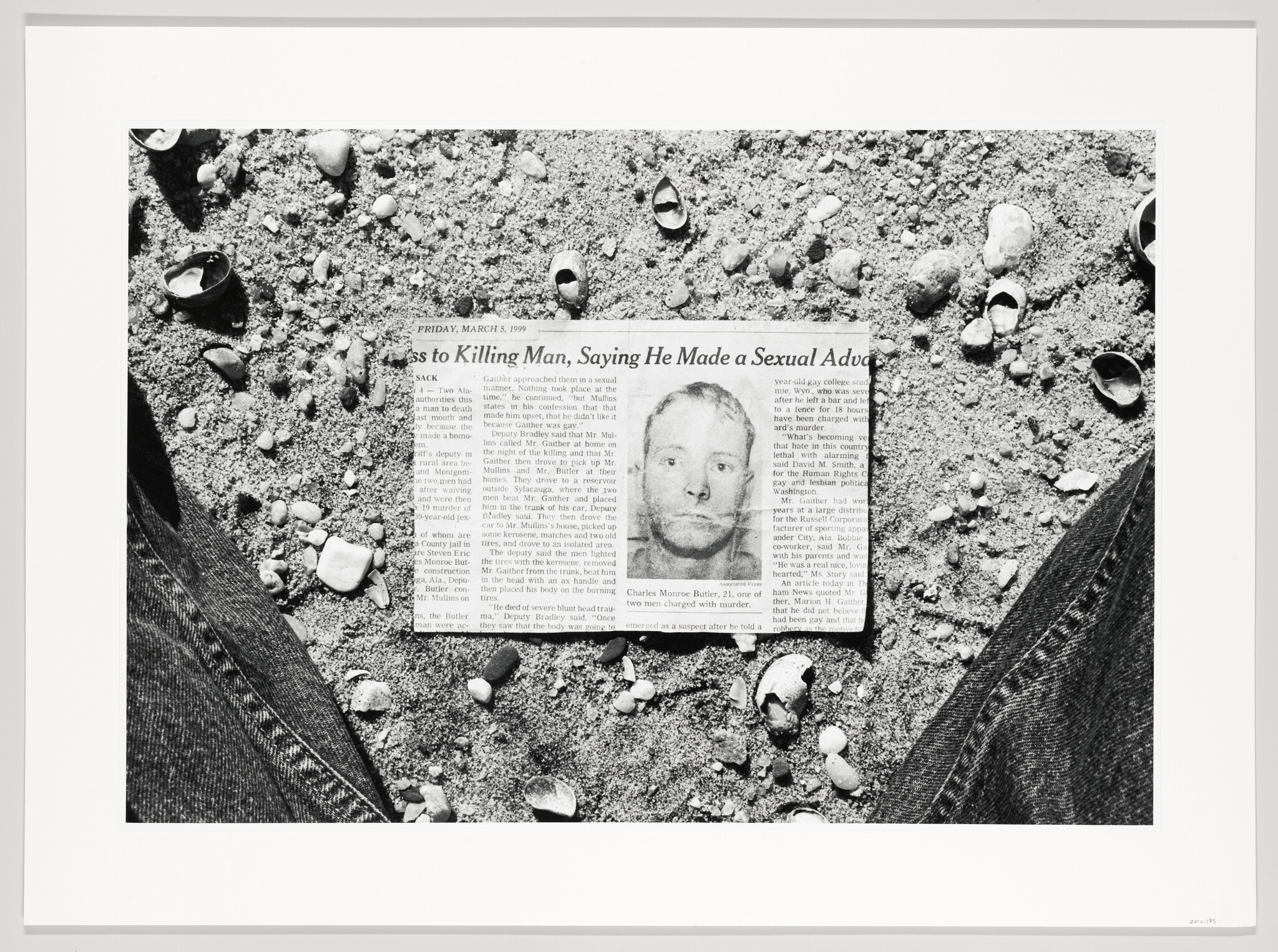 A black and white photograph of a newspaper article lying on the ground surrounded by small rocks and shells. The article features a headline about a man confessing to a killing and includes a mugshot of a person. The date "Friday, March 5, 1999" is visible at the top of the article. The edges of a pair of jeans frame the bottom corners of the image.