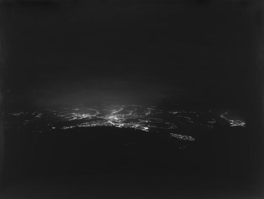 Aerial night view of a city with scattered street and building lights across the landscape.