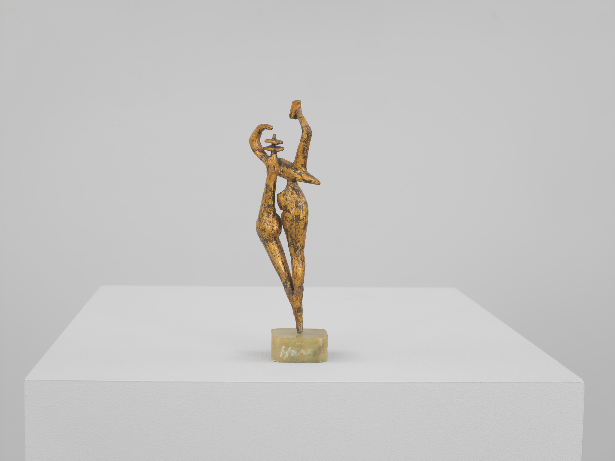 A small bronze abstract sculpture of two elongated figures entwined in a dance on a pedestal.