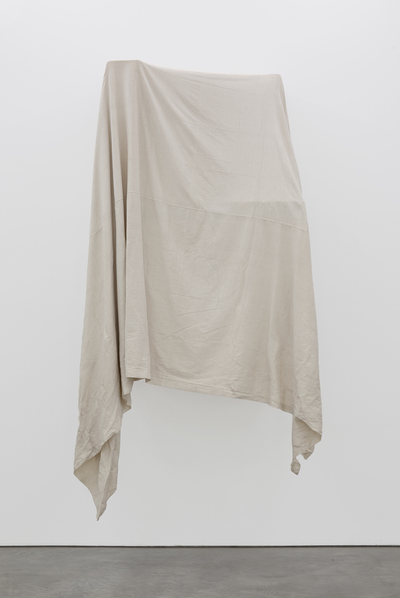A large beige cloth hangs draped on a white wall with two hanging corners.