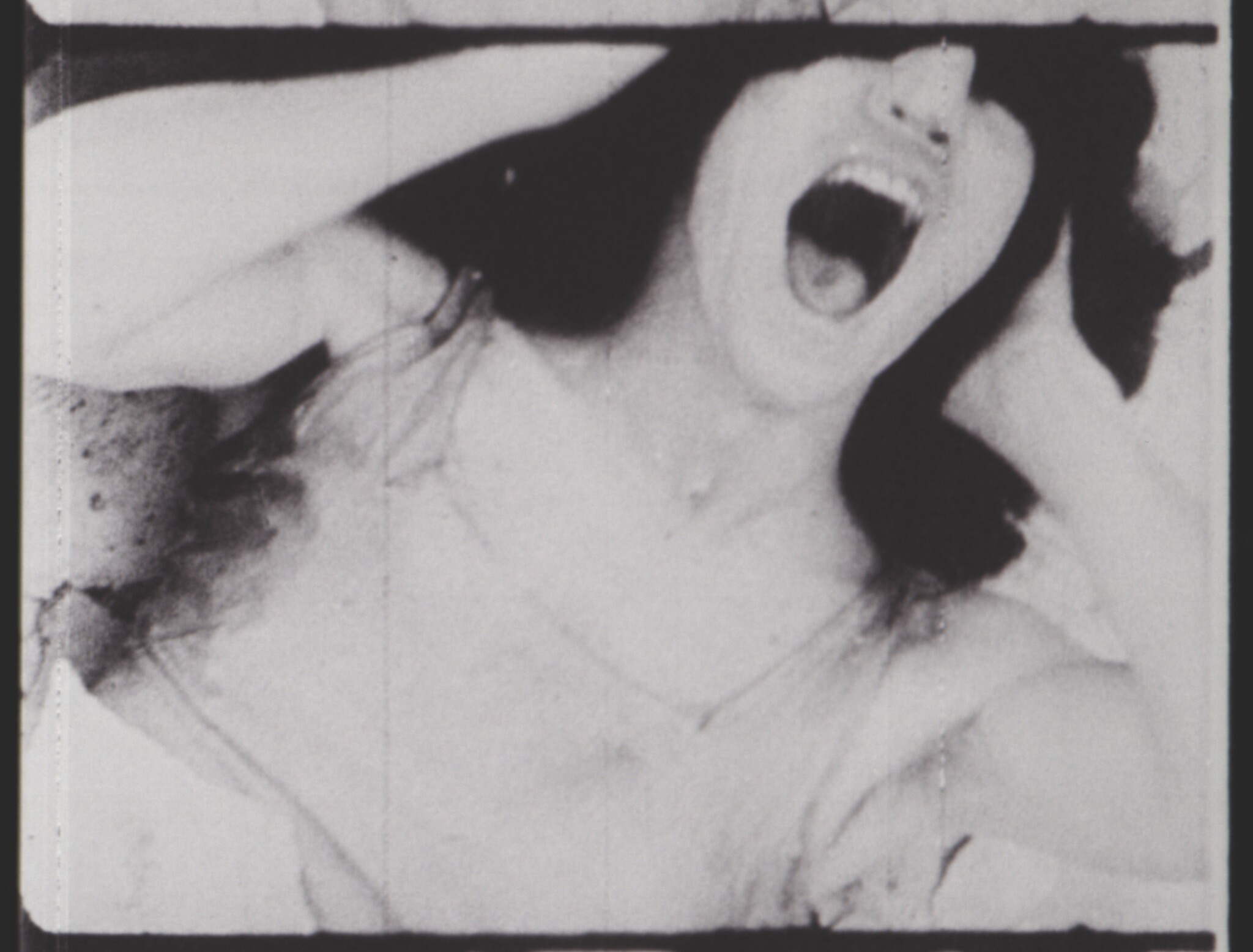 A woman screams with her mouth wide open and hands clutching her head in black and white.