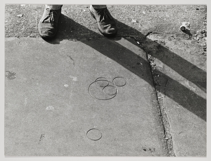 A person stands at the edge of a sidewalk casting long shadows over scattered rubber bands.