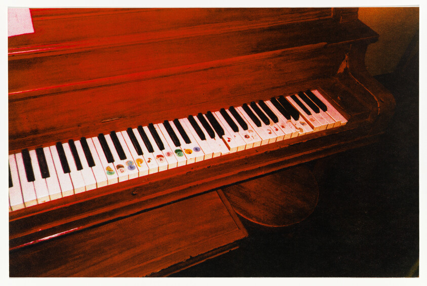 A worn wooden piano keyboard with colorful stickers on several white keys.