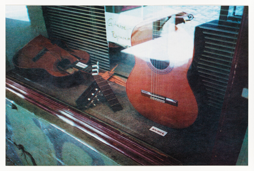 Two acoustic guitars displayed in a glass case, one with its neck detached and lying beside it.
