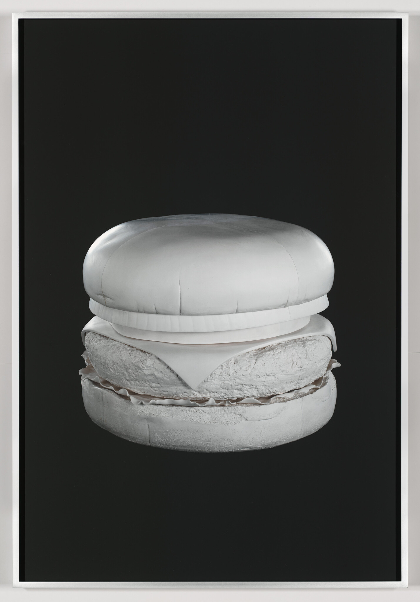 A monochrome white hamburger sculpture showing bun, cheese, and patty against a black background.