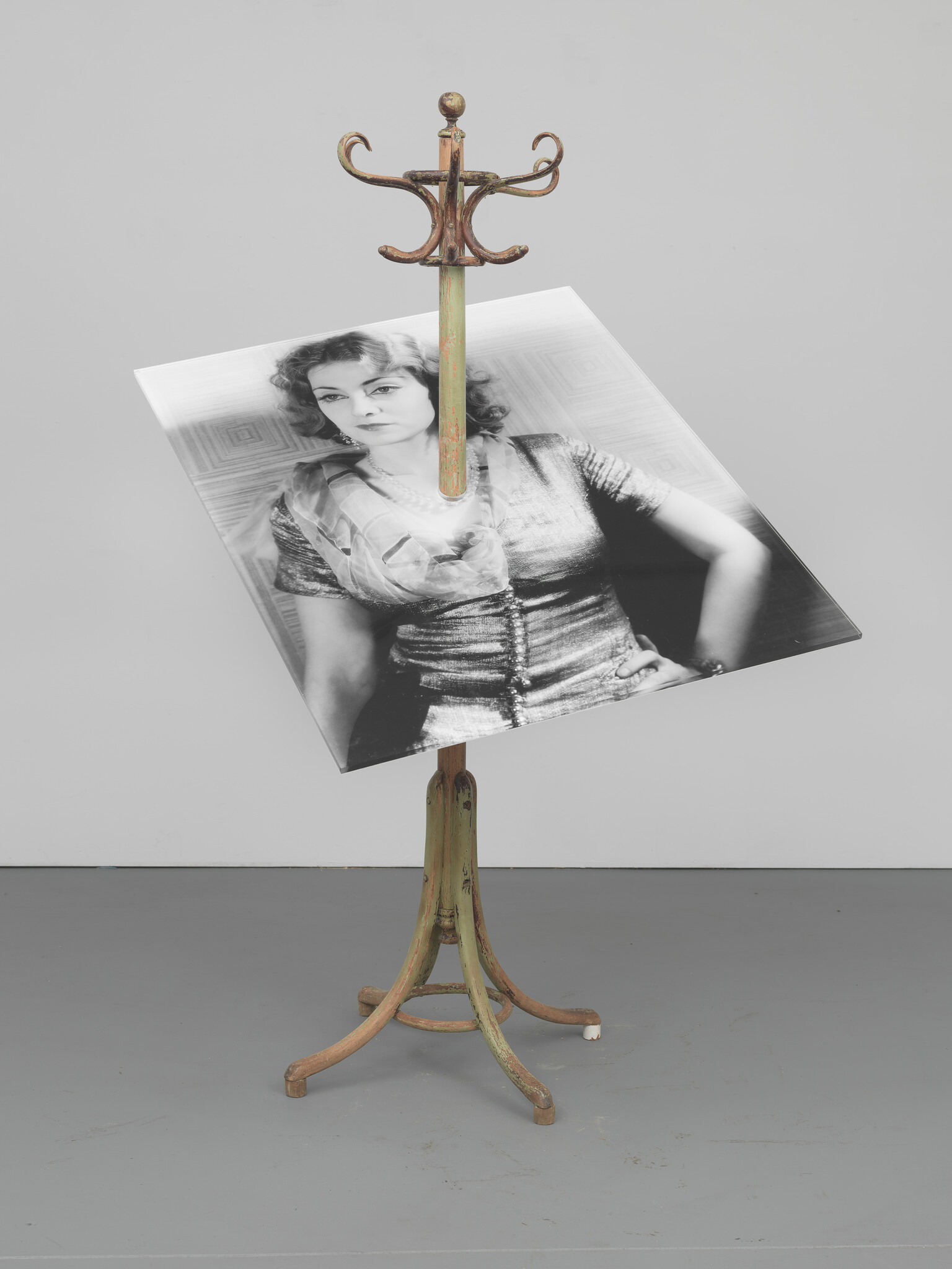 A wooden coat rack displays a large tilted black-and-white portrait of a woman.