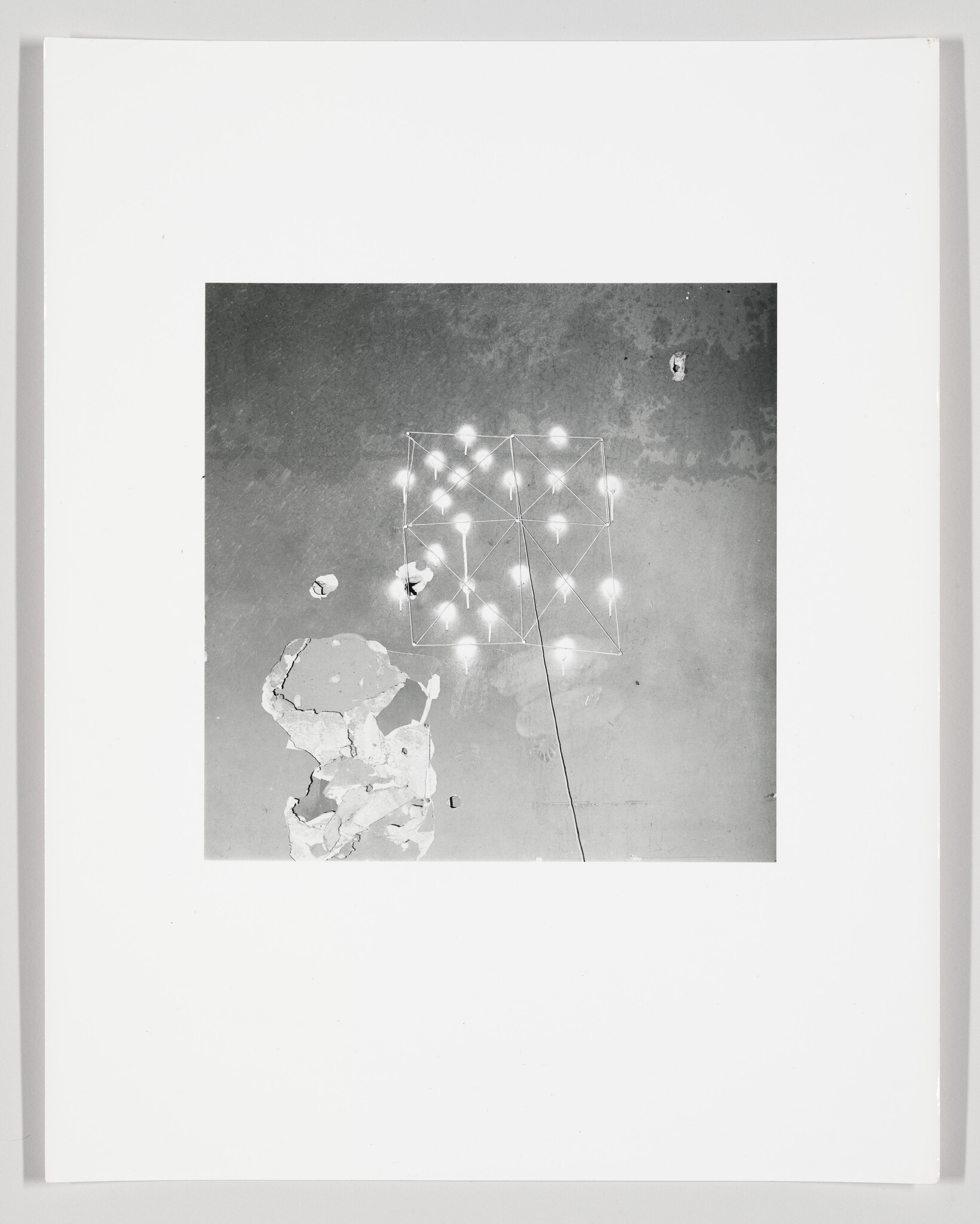 Square photograph shows a grid of glowing bulbs mounted on a pole above peeling wall plaster.