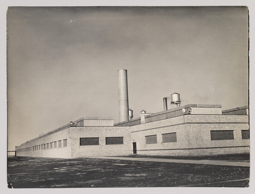 Large brick industrial factory building with a tall smokestack and rooftop water towers.