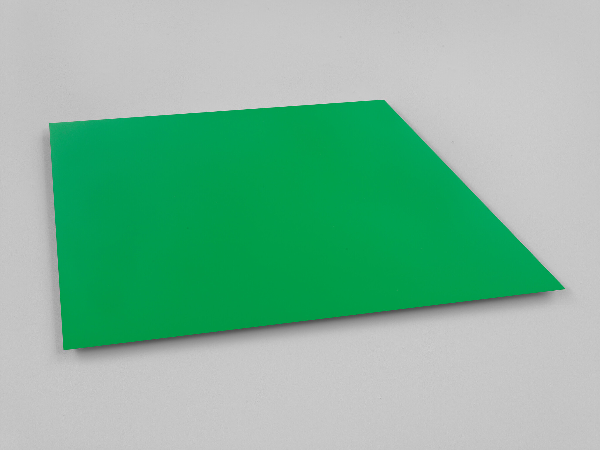 A bright green, rectangular sheet of paper or cardstock is tilted at an angle against a white background.
