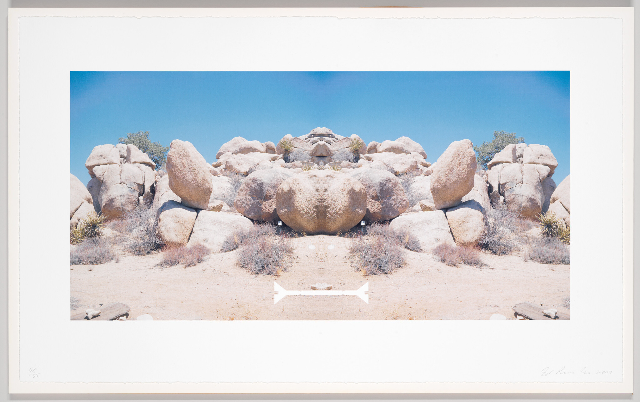 Symmetrical sunlit boulder formation in a dry desert landscape under a clear blue sky.
