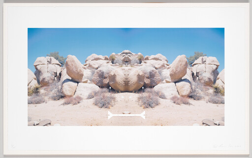 Symmetrical sunlit boulder formation in a dry desert landscape under a clear blue sky.