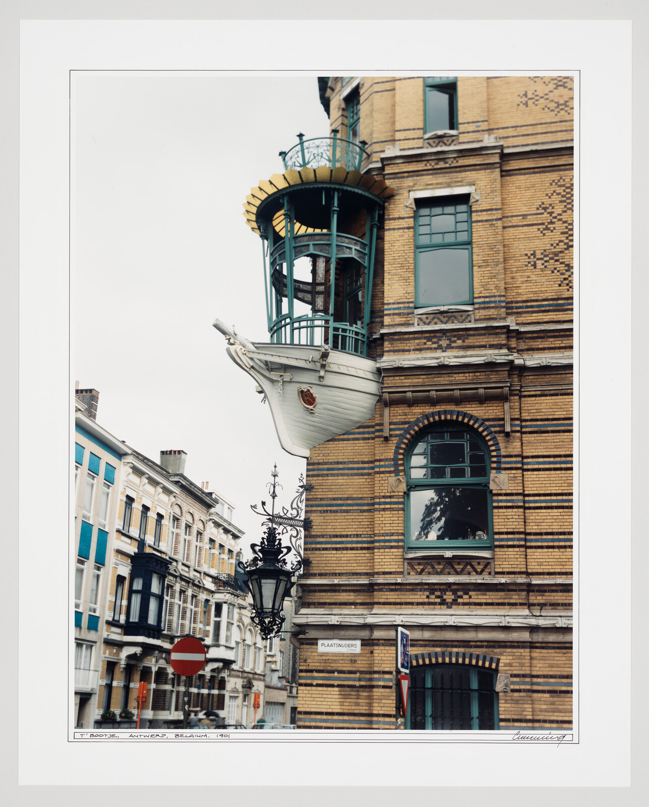 A small white ship-shaped balcony juts from a yellow brick building above the street.