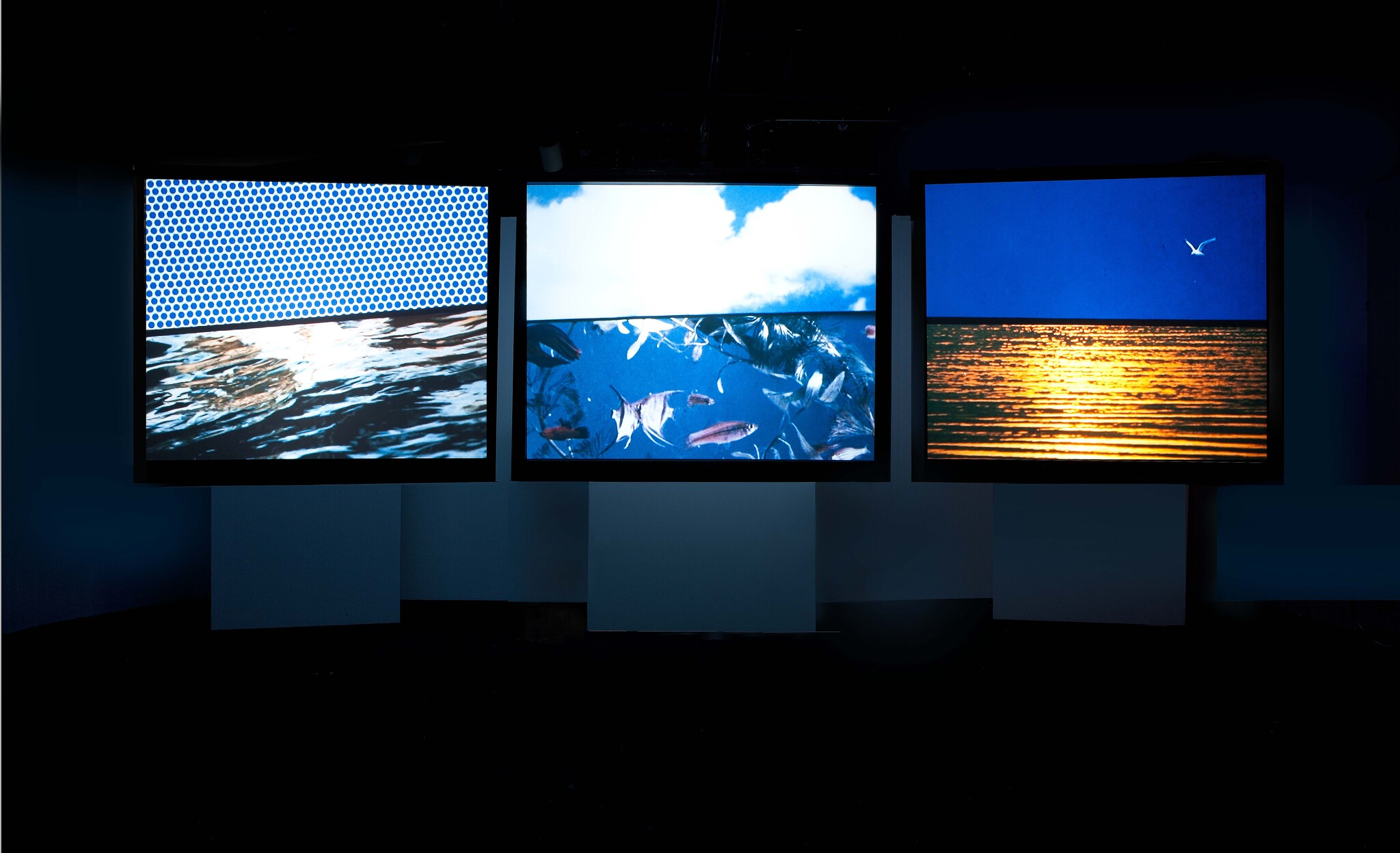 Three illuminated screens show ocean scenes: dotted water, fish underwater, and golden sunset with a bird.