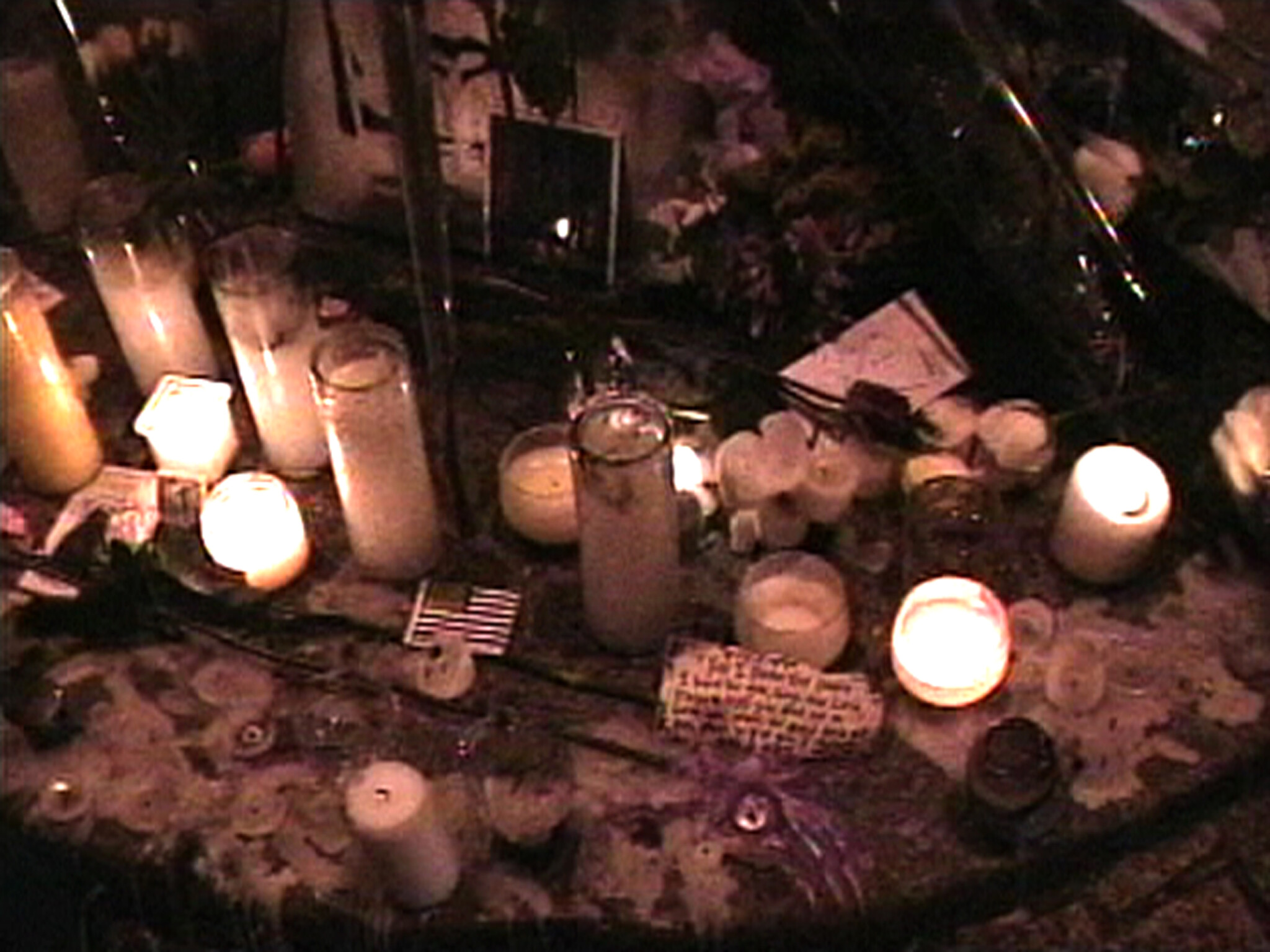 Several lit candles and flowers arranged closely together as part of a nighttime memorial.