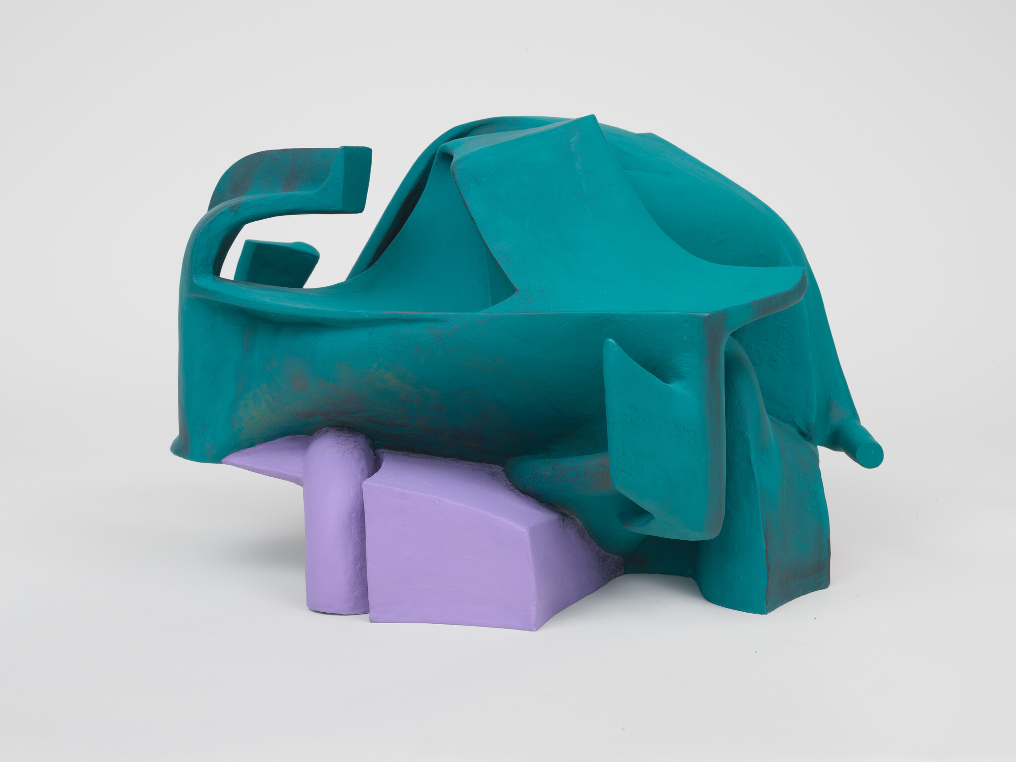 A teal abstract sculptural form rests on a lavender geometric base against a white background.