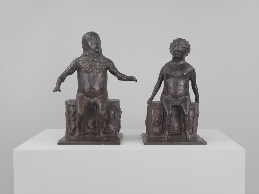 Two small bronze seated figures with different head textures resting on carved rectangular bases.