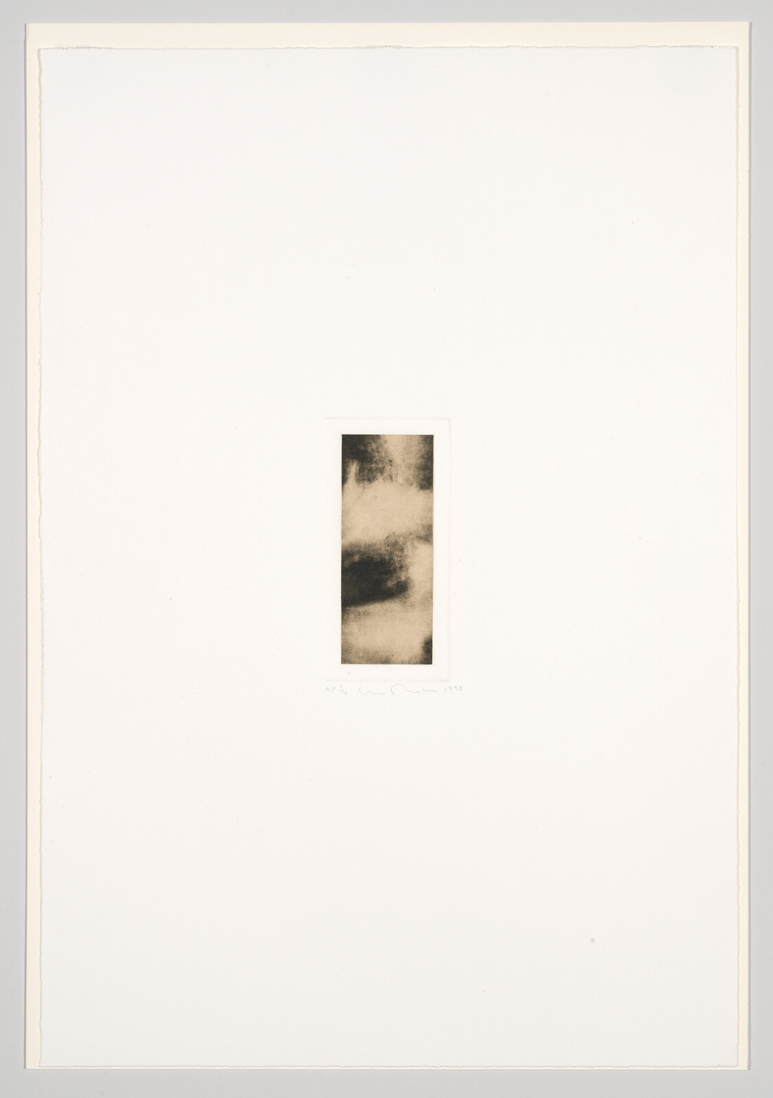 A minimalist artwork featuring a small, abstract, monochromatic print centered on a large white mat. The print contains shades of black and gray, creating a smoky or cloudy effect. There is a signature and edition number at the bottom left corner on the mat.