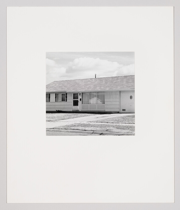 A small single-story suburban house with a front lawn, driveway, and closed blinds on the window.