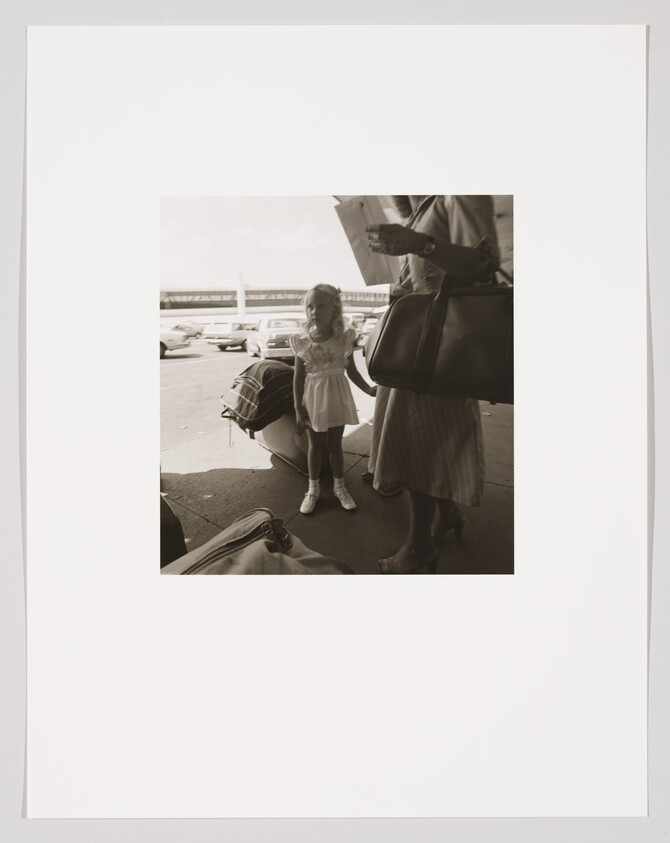 A young girl holding an adult's hand beside luggage at an airport curb.